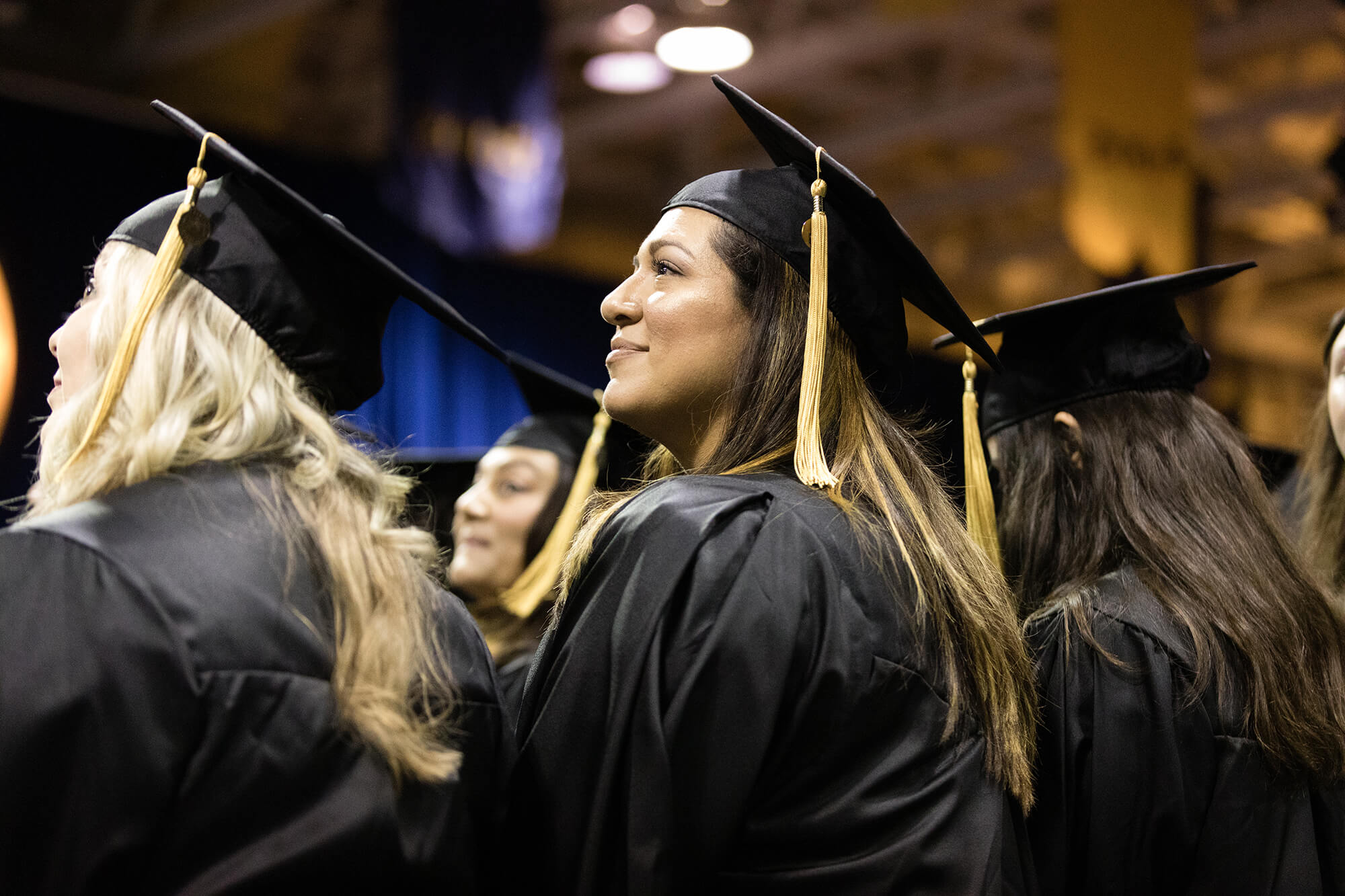 A graduate smiles at her family in the crowd during a commencement ceremony.